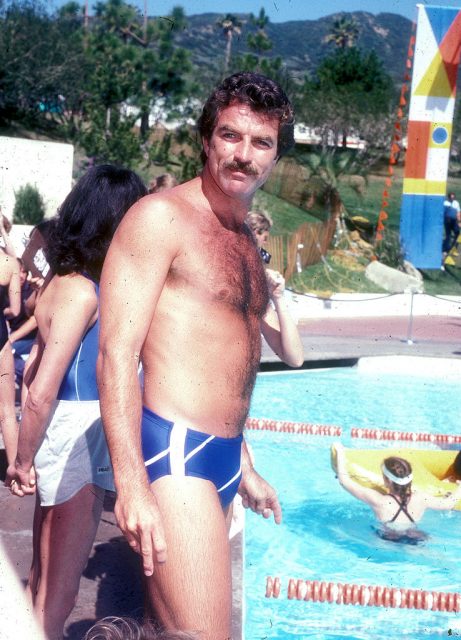 Tom Selleck standing by a pool in a speedo
