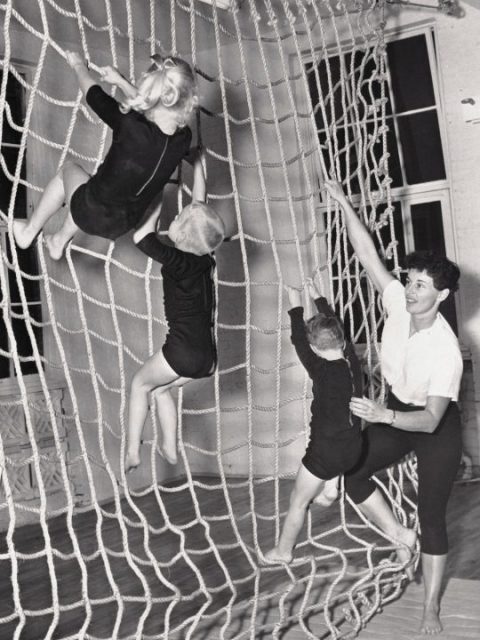 children in a 1950s PE class climb netting.