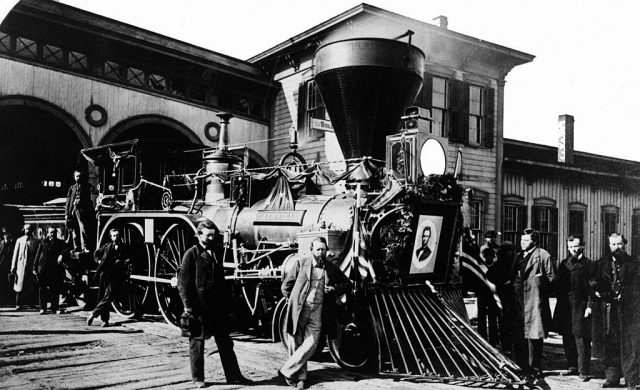 Men standing around a train with Abraham Lincoln's portrait