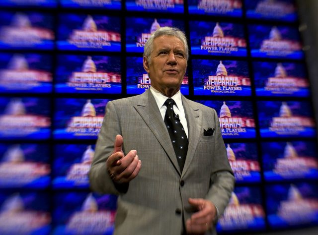 Alex Trebek standing in front of the Jeopardy! clue board