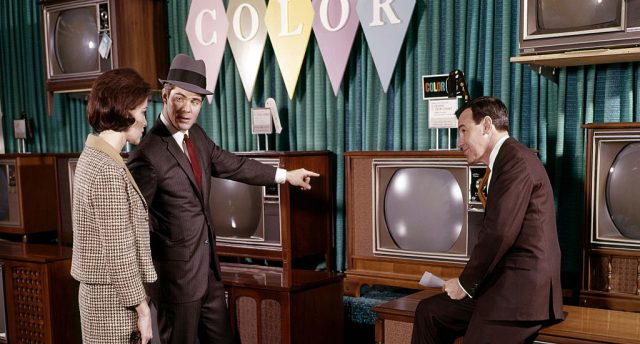 Two men and a woman standing in front of vintage television sets