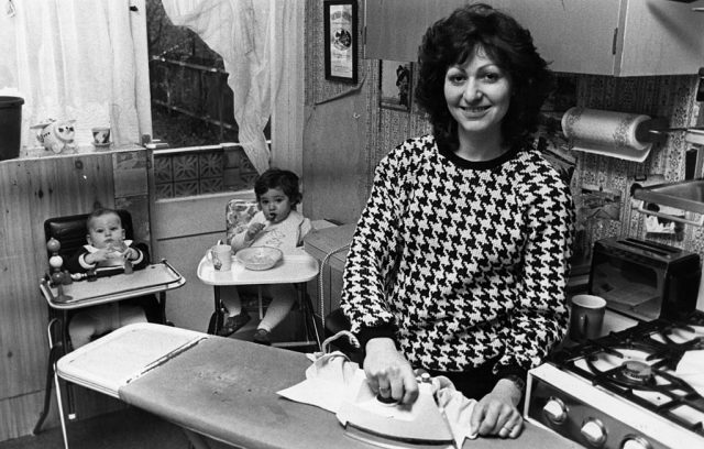 A mother ironing clothes while her two babies sit in high chairs