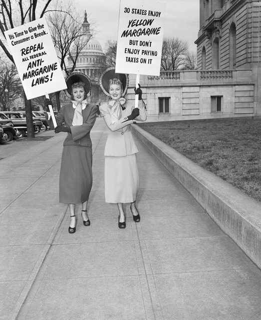Two housewives in blue bonnets add their bit towards the fight for repeal of the tax on oleomargarine. They parade with their signs near the Capitol. (Photo Credit: Bettmann / Contributor)