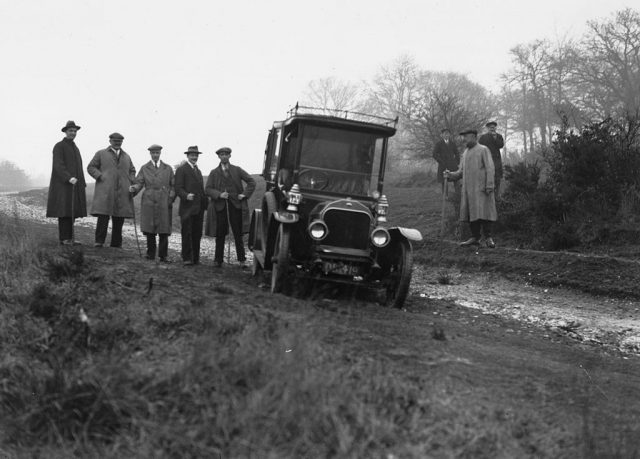 Police officers standing around a car parked along a dirt road