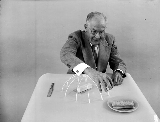 circa 1955: American amateur inventor Russell E Oakes demonstrates his ‘sleeve protector’ which covers a slab of butter to prevent him accidentally touching it as he leans across a table. (Photo Credit: Evans/Three Lions/Getty Images)