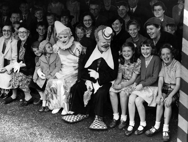 Two clowns sitting amongst a crowd of children