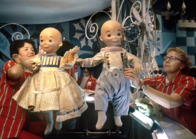 Two female Disneyland employees holding dolls from the It's a Small World ride