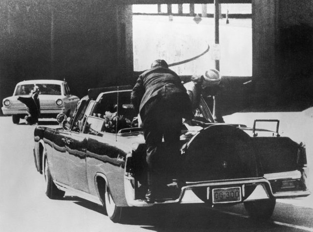 Secret Service agent leaning over the back of John F. Kennedy's car