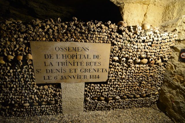 Sign in front of a wall made from human skulls and femurs