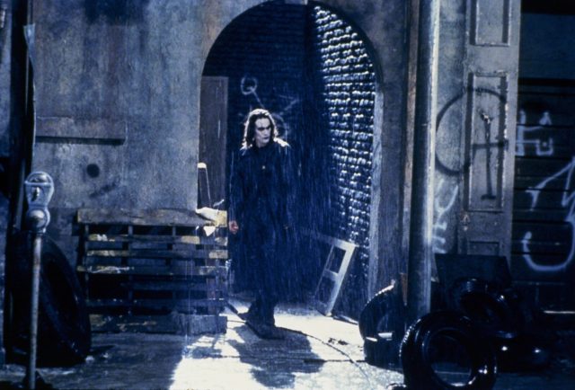 Eric Draven walking through an arched doorway on a rainy night