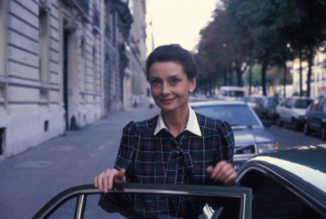 Audrey Hepburn standing behind an open car door