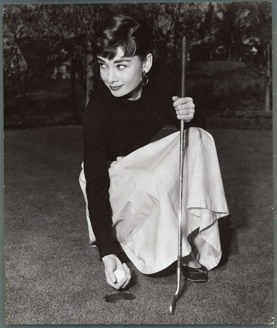 Audrey Hepburn leaning over to pick up a golf ball