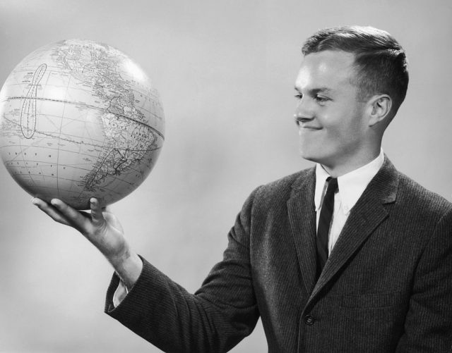 Portrait of a young man, wearing a suit and tie, holding a globe in one hand. (Photo Credit: Lambert/Getty Images)
