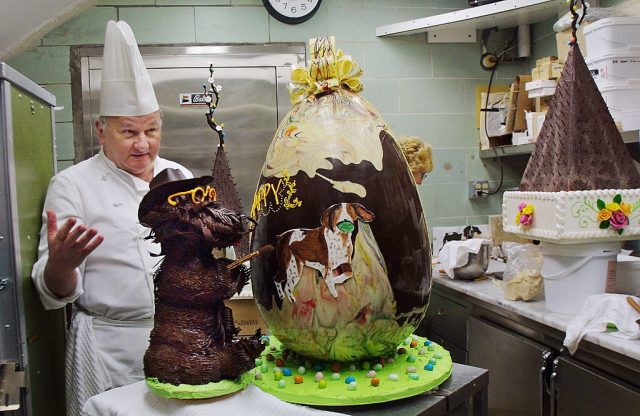 White House Pastry Chef Roland Mesnier presents his creation, a 40-pound semi-sweet chocolate Easter Egg decorated with the First Family’s pet dogs Barney (L) and Spot in the White House kitchen March 29, 2002 in Washington, DC. (Photo Credit: Manny Ceneta/Getty Images)
