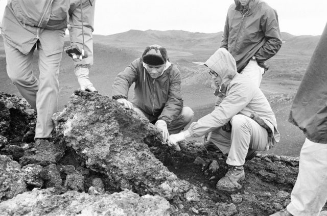 NASA astronauts kneeling around a large rock