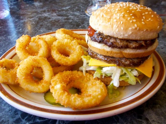 Double-decker hamburger on a plate with onion rings