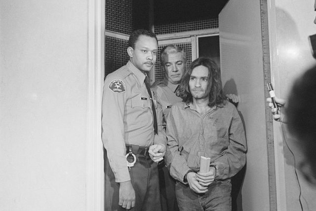 Charles Manson being led into a room by two police officers