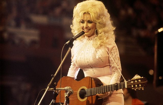 Dolly Parton standing behind a microphone with a guitar