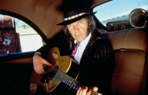 Neil Young sitting in a car with a guitar