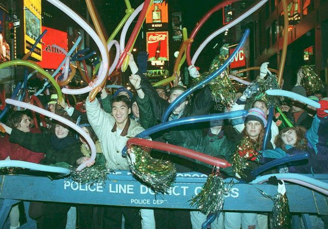 Crowd gathered behind a barrier, waving balloons and holding tinsel