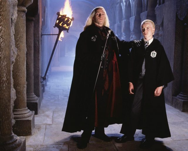 Lucius Malfoy standing with his hand of Draco Malfoy's shoulder