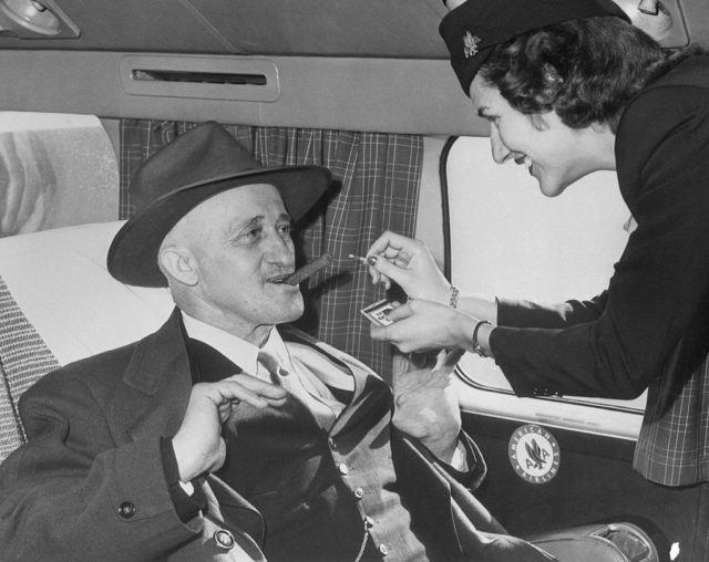 A man having his cigar lit by a stewardess 