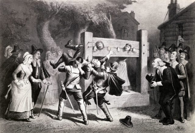 Two accused witches with their heads and hands locked, while their accusers look on