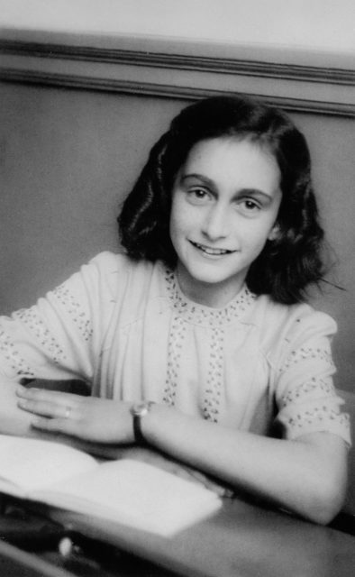 Anne Frank sitting at a desk with her arms folded