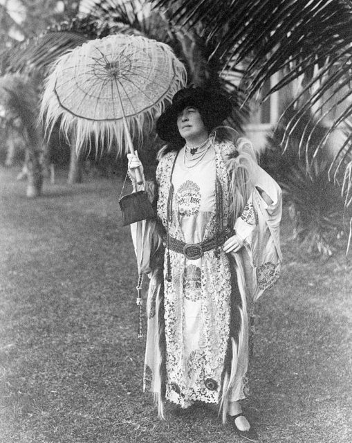 Margaret Brown stands under a palm tree with parasol.