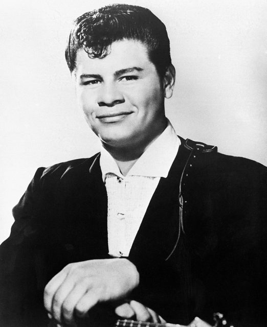 Ritchie Valens with his hands resting on his guitar 