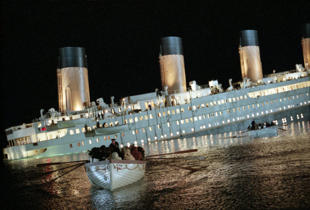The Titanic is sinking while lifeboats filled with passengers row away from the disaster.