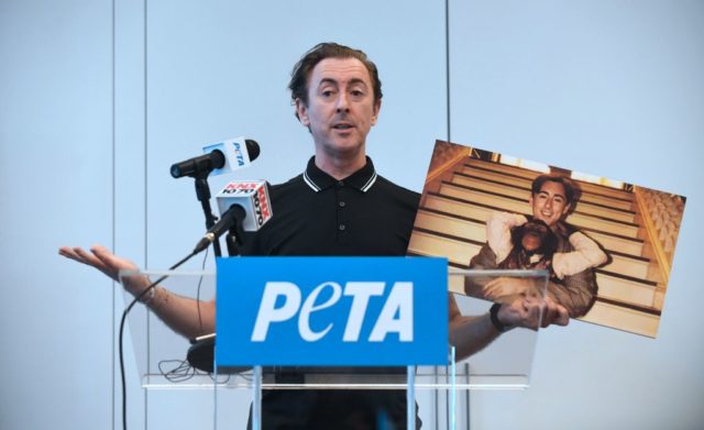 Alan Cumming holding a picture of him and Tonka the Chimpanzee