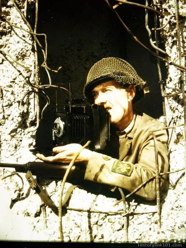 Combat cameraman has been in the ETO 27 months. He uses an old shattered German pillbox for protection while photographing the war action.