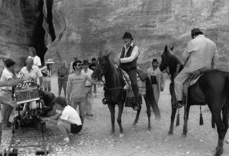 George Lucas readies a scene with Sean Connery and John Rhys-Davies on horseback in the canyon in Petra, Jordan for the third film, Indiana Jones and the Last Crusade (1989).