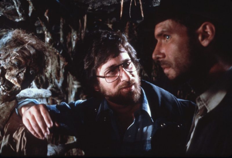 Spielberg chats with his star, Harrison Ford, while a decomposed friend looks on