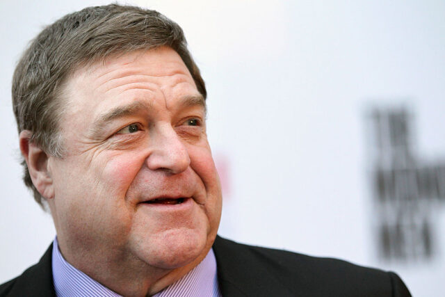 John Goodman standing on a red carpet