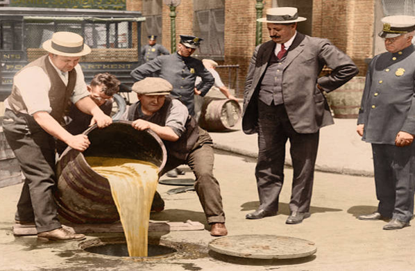 New York City Deputy Police Commissioner John A. Leach (right) watches as agents pour liquor into a sewer following a raid during the height of Prohibition