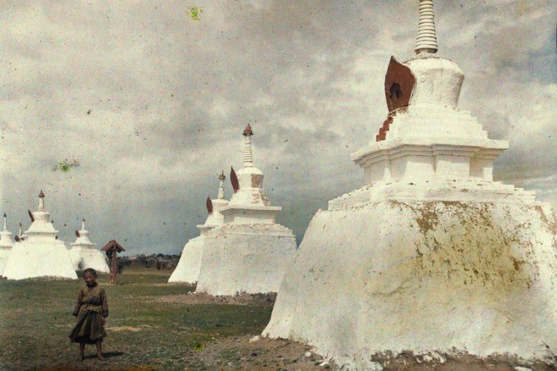 A tiny monk stands near a stupa, which is a holy Buddhist reliquary.