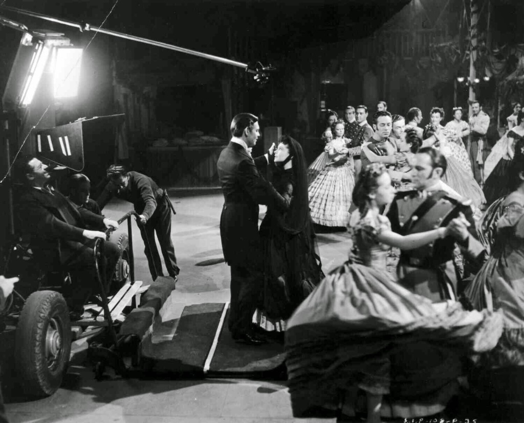Clark Gable as Rhett Butler and Vivien Leigh, dancing. Both are standing on a movable floor, being watched by dancers and director George Cukor, before he left production.