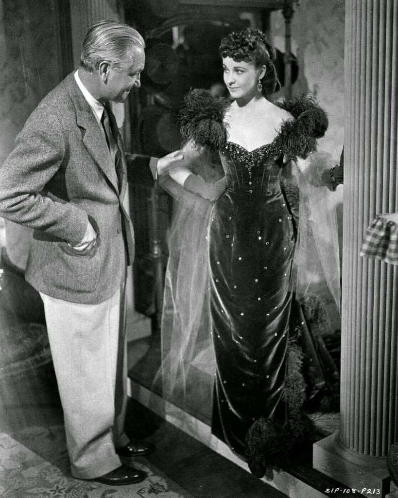 Director Victor Fleming looking at Vivien Leigh as Scarlett O'Hara, who is standing in doorway, wearing red gown.