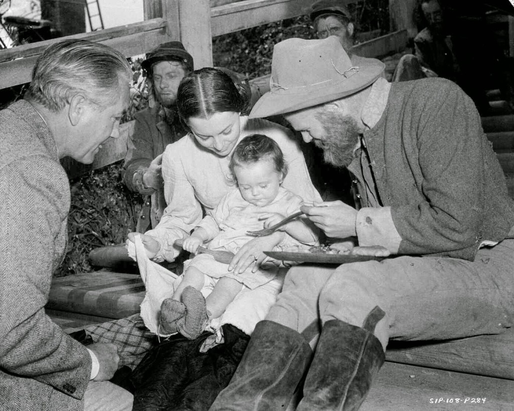 Olivia De Havilland as Melanie Hamilton, with Ric Holt as Beau Wilkes (11 months) seated on her lap. Seated alongside is Phillip Trent as a hungry solider, and director Victor Fleming.