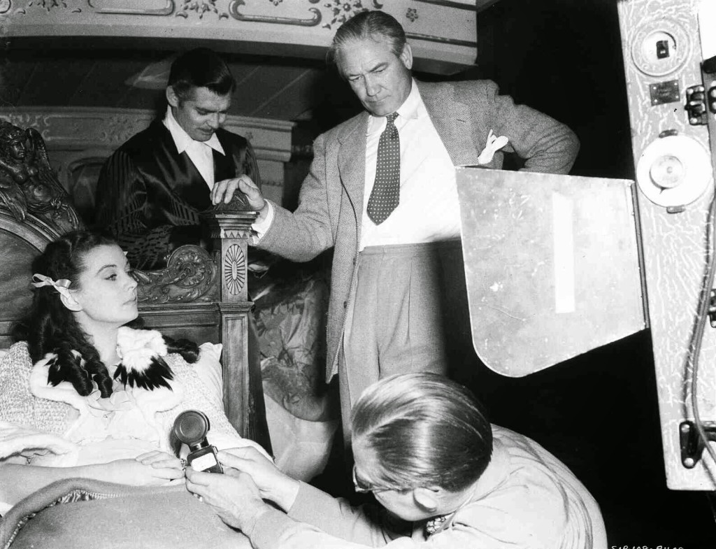 Vivien Leigh as Scarlett O'Hara laying in bed, Clark Gable as Rhett Butler, director Victor Fleming and man holding light meter.