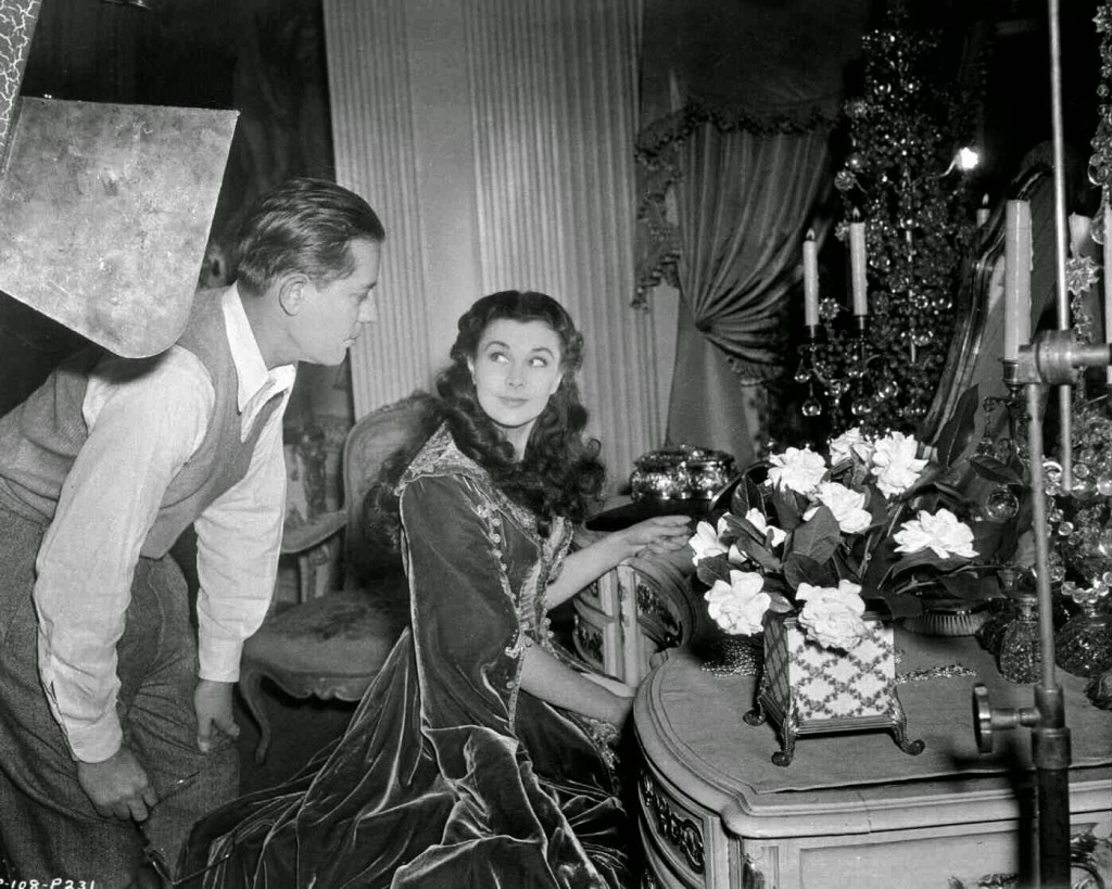 Vivien Leigh as Scarlett O'Hara, seated at dressing table, with lighting man leaning over sholder.