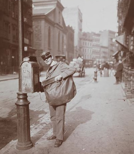 A letter carrier standing in front of a mailbox at Mott Street above Park Row, 1903