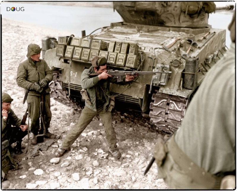 Taking cover behind their M4A3E8 Sherman tank escort, one man of this Ranger patrol of the 5th Regimental Combat Team, US 24th Infantry Division, uses his M1918A2 BAR to return the heavy Chinese Communist small arms and mortar fire which has them pinned down on the bank of the Han River. At left another soldier uses a field radio to report the situation to headquarters. 23 February 1951 (Source - NARA FILE#: 111-SC-358782) (Colorised by Doug)
