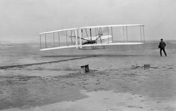 First flight of the Wright Flyer I, December 17, 1903, Orville piloting, Wilbur running at wingtip.