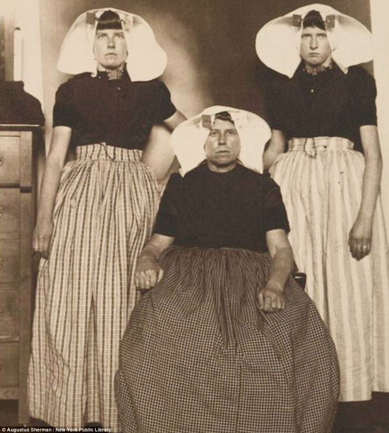 Three unsmiling Dutch women show off their traditional head gear and long skirts while they were detained on Ellis Island 