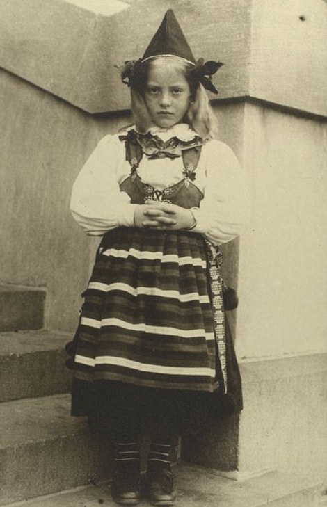 A young Swedish girl in traditional pointed hat and elaborate costume is pictured on Ellis Island while her family wait to be approved to travel to the mainland 