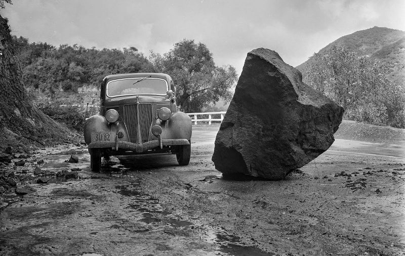 A boulder on a road after a rainstorm on March 1, 1938. The car may be the photographer's vehicle; no other information was available.