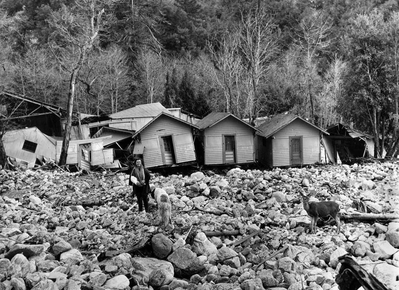 March 6, 1938 Ruth Curry, with a broken arm, owner of Camp Baldy resort, stands in front of shattered cabins after floodwaters destroyed the majority of them